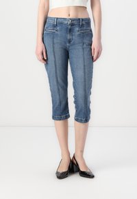 Pantalon en denim bleu court avec une coupe ajustée, comprenant des poches avant, des détails cousus et des ourlets retroussés.