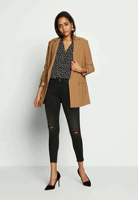 Brūns žakets pār melnu punktu blūzi, kombinēts ar melniem plīsušiem skinny džinsiem un melnām augstpapēžu kurpēm. Minimāli aksesuāri.