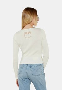 Maglione bianco a coste con un motivo grafico marrone chiaro sul retro, abbinato a jeans blu chiaro. La vestibilità è slim e contemporanea.