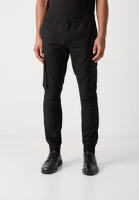 Czarne spodnie cargo z elastycznym paskiem w talii, dopasowanymi mankietami i bocznymi kieszeniami. Wykonane z lekkiego materiału o gładkiej fakturze.