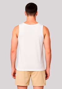 Weißes ärmelloses Tanktop aus glattem Stoff, mit rundem Ausschnitt und lässiger Passform, kombiniert mit khakifarbenen Shorts.