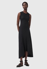Abito nero senza maniche in costina, con un corpetto attillato e un orlo asimmetrico. Indossato con sandali neri e orecchini a cerchio minimalisti in oro.