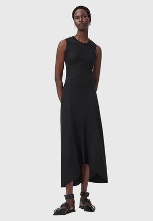 Abito nero senza maniche in costina, con un corpetto attillato e un orlo asimmetrico. Indossato con sandali neri e orecchini a cerchio minimalisti in oro.