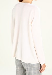 Ljusrosa långärmad tröja med lös passform, rundad halsringning och ribbstickade ärmslut, parat med rutiga grå byxor. Mjuk textur.