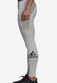 Vaaleanharmaat urheilulegginsit, jotka on valmistettu joustavasta kankaasta. Niissä on musta Adidas-logo vasemmassa pohkeessa ja kapea istuvuus.