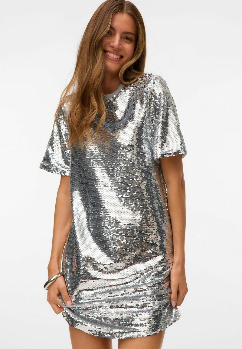 Vestito corto in paillettes argento con maniche corte, vestibilità rilassata e orlo leggermente arricciato. La texture lucida riflette la luce, aggiungendo interesse visivo.