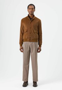 Brown suede bomber jacket with a high collar, button closure, and two front pockets; paired with beige trousers and dark shoes.