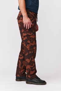 Brune camouflage cargo bukser med multiple lommer, lavet af robust stof, med elastisk talje og tapered ben, båret med sorte sko.