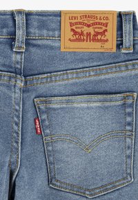 Poche arrière d'un jean Levi's bleu clair avec l'étiquette rouge emblématique de Levi's et un patch en cuir tan de la marque montrant deux chevaux et du texte.