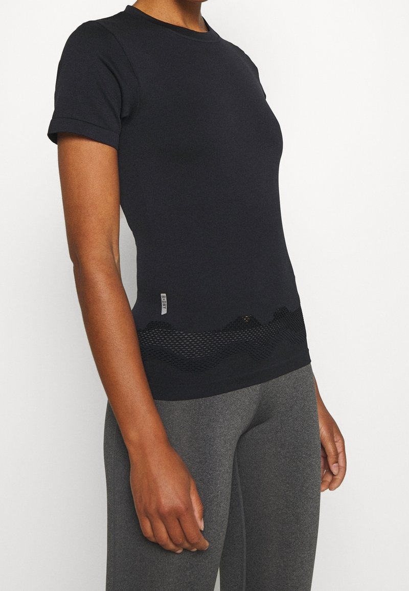 Camiseta negra de manga corta hecha de material suave, con un panel de malla en la cintura que presenta un patrón de olas. Combinada con leggings grises.
