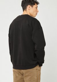 Felpa nera con scollo rotondo, maniche lunghe e vestibilità rilassata, realizzata in tessuto morbido con polsini e orlo a coste.