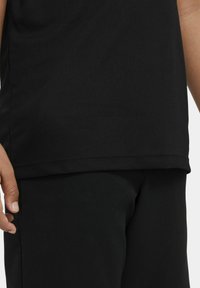 Svart idrottstopp och byxor med slät, matt yta och en åtsittande design. T-shirten har en rak nederkant och korta ärmar.