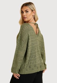 Grön stickad tröja med v-ringning och detalj med bakband. Har ett hålmönster och långa ärmar, med en texturerad finish.