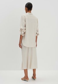 Beige Langarmshirt mit aufgekrempelten Ärmeln, abgerundetem Saum, kombiniert mit einem passenden Midirock mit seitlichen Schlitzen und einer glatten Textur.