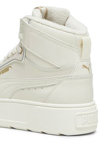 Białe sneakersy typu high-top z podszewką z sztucznego futra, teksturowana syntetyczna cholewka, złote akcenty, detal z logo oraz masywna biała gumowa podeszwa.