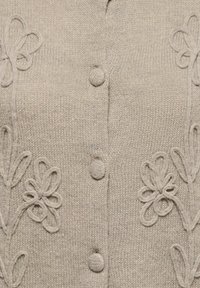 Tissu beige tricoté avec des motifs floraux en torsades et des boutons recouverts disposés verticalement au centre.
