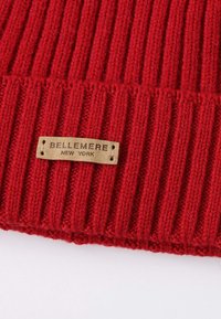 Red ribbed knit beanie with a textured surface and a beige leather label featuring embossed text "BELLEMER" and "NEW YORK."