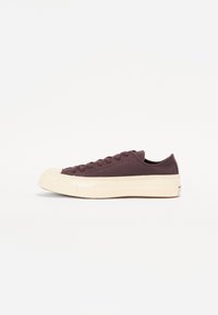 Baskets basses avec une tige en toile marron foncé, une semelle en caoutchouc crème, un bout rond et six œillets pour les lacets. Design minimaliste.