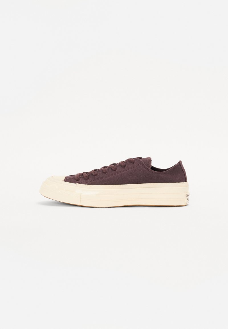 Baskets basses avec une tige en toile marron foncé, une semelle en caoutchouc crème, un bout rond et six œillets pour les lacets. Design minimaliste.