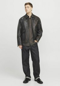 Chaqueta de cuero negra con dos bolsillos frontales, combinada con una camisa de botones oscura, jeans de mezclilla oscuros y zapatos negros.