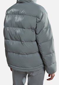 Grå, puffjakke med en blank overflade, der har vandret kanaler og en høj krave, set fra ryggen.