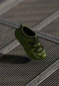 Zielony but sportowy z teksturowaną cholewką, elastycznymi sznurówkami i amortyzowaną podeszwą. Projekt charakteryzuje się zaokrąglonym noskiem i pętlą u pięty.