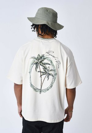 Camiseta de gran tamaño color crema con un gráfico de palmera dentro de un diseño circular y el texto "Project X Paris" en la parte trasera.