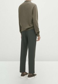 Sweter oliwkowozielony z okrągłym dekoltem, w zestawieniu z ciemnoszarymi spodniami i białymi sneakersami. Miękka faktura, luźny krój, minimalistyczny design.