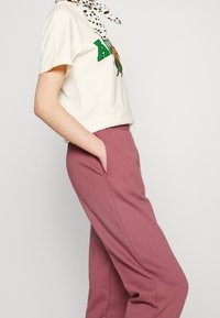 Kermakuvioinen t-paita vihreällä painatuksella edessä, yhdistettynä pinkkeihin verkkareihin, joissa on sivutaskut ja elastinen vyötärö.