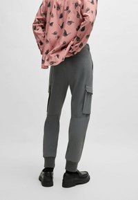 Graue Cargo-Hosen mit gerippter Textur und elastischen Bündchen, ausgestattet mit Seitentaschen. Kombiniert mit einem rosa Longsleeve-Shirt mit Schmetterlingsdruck.