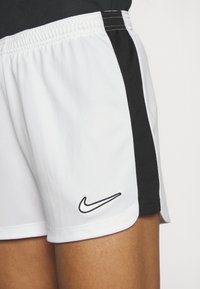Nike sportos rövidnadrág fehér testtel és fekete oldalsó panelekkel. Rugalmas derékpánttal és hímzett logóval rendelkezik a bal oldalon.