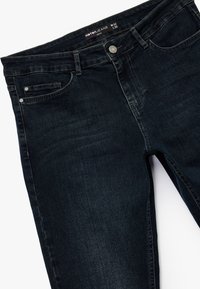 Vaqueros azul oscuro de denim con una textura suave. Presenta un bolsillo delantero, trabillas para cinturón y un cierre de botón en la cintura.