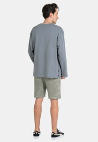 Gray long-sleeve shirt with a relaxed fit, paired with light green shorts, worn with black and white sneakers. Casual, soft fabric texture.