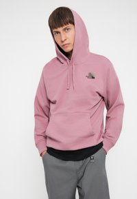 Pullover hoodie i støvet pink med snøre og kengurulomme. Broderet logo på brystet. Glat, mellemtykt stof.
