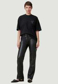 Black oversized T-shirt with short sleeves, paired with fitted black faux leather pants. Plain design, matte texture, and no visible patterns.