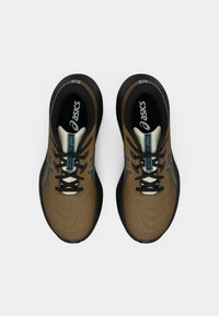 Zapatillas deportivas marrones con una parte superior texturizada, suelas negras, acentos en color aguamarina y cordones negros. Cuentan con un diseño contorneado para mayor comodidad.