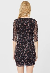 Robe courte noire à fleurs avec manches longues transparentes et froncées. Présente une silhouette ajustée ornée de petits motifs floraux multicolores.