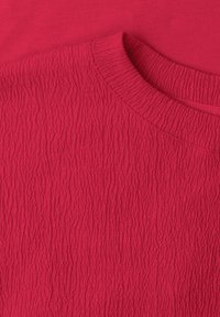 Gros plan d'une chemise rouge en tissu texturé avec un col rond côtelé sur un fond rouge uni.