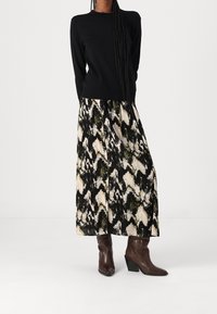 Zwart langemouwen top gecombineerd met een gemusterde maxi rok in tinten groen, zwart en crème. Afgemaakt met bruine haklaarzen.