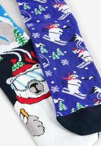 Calze lavorate a maglia con una base bianca che presenta un orso polare e un'anatra grigia, e un paio blu decorato con pupazzi di neve che sciano e alberi.