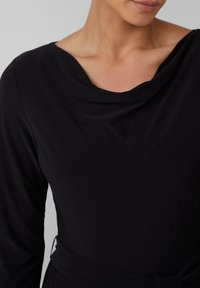 Vestito nero a maniche lunghe con scollo drappeggiato, tessuto morbido e silhouette aderente; include un dettaglio in vita legato.