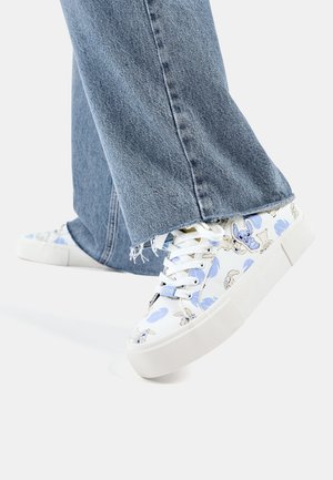 Hvide platformsneakers med blå blomsterprint og tegneseriefiguren Stitch, brugt med slidte blå jeans med frynsete kanter.