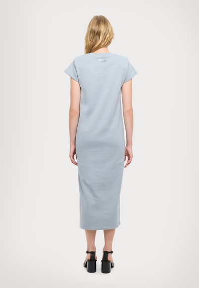 Vestido azul claro hasta la rodilla con mangas cortas, un corte holgado y detalles de costura sutiles. Combinado con sandalias negras de tacón cuadrado.