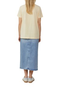 Lichtbeige katoenen t-shirt gecombineerd met een lichtblauwe denim midi-rok. De rok heeft een rechte snit en is enkel-lang. Casual schoeisel wordt gedragen.