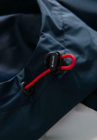 Marineblå stof med en snor med rød accent og sorte stop for justeringer. Glat tekstur med subtil glans.