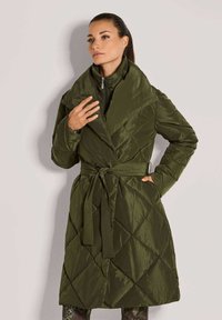 Olijfgroen gewatteerde lange jas met een brede kraag, een ceintuur in de taille en een diagonale stikpatroon, gemaakt van een soepele, glanzende stof.