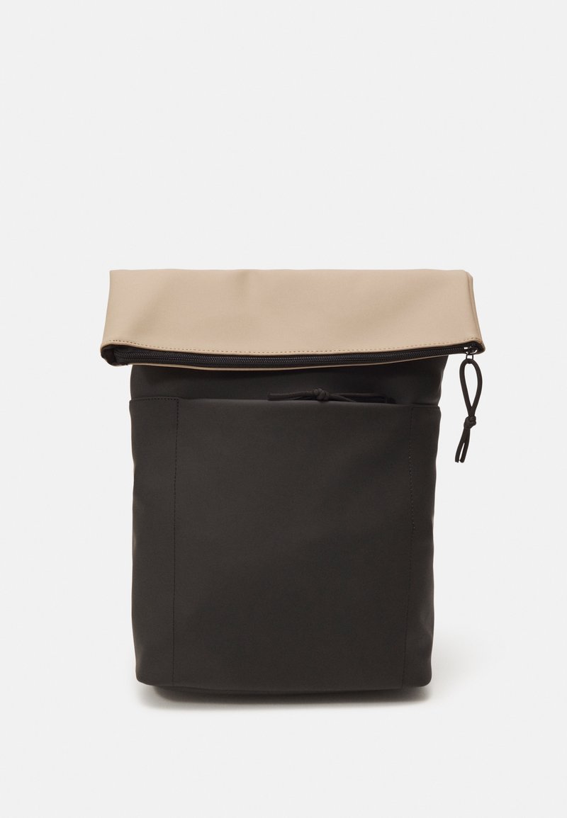 Sac à dos noir avec un rabat beige et une poche frontale, équipé d'une fermeture éclair et d'une languette de tirage sur le bord supérieur.