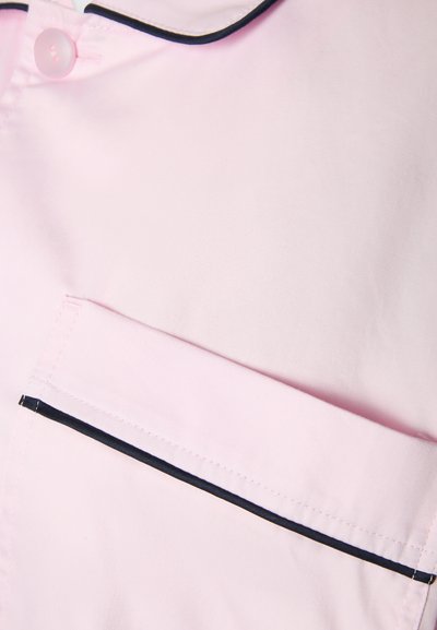 Ροζ ύφασμα με γιακά με κουμπιά και τσέπη περιμετρικά με μαύρο περίγραμμα, παρουσιάζοντας λεπτομέρεια από κοντά.