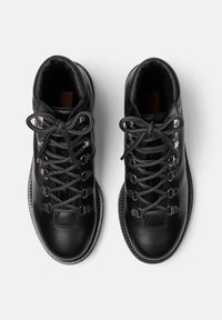 Botas de senderismo de cuero negro con cordones grises, ojales de metal y cuello acolchado. Suela texturizada y un diseño elegante y redondeado.