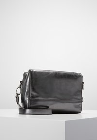 Czarna skórzana torebka na ramię o prostokątnym kształcie, gładkiej fakturze i regulowanym pasku. Posiada subtelne oznaczenia marki oraz metalowe akcenty.